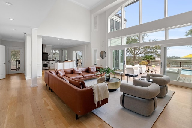 living area with light wood-style floors, recessed lighting, crown molding, and a high ceiling