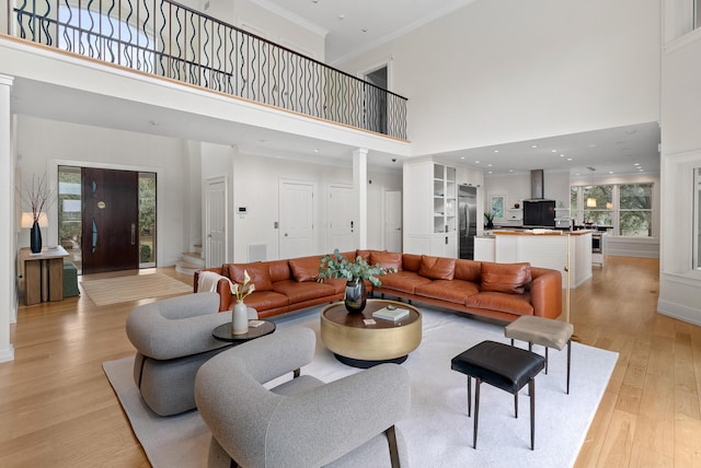 living area featuring a towering ceiling, ornamental molding, stairway, light wood finished floors, and decorative columns