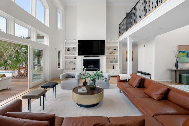 living area featuring crown molding, a fireplace, wood finished floors, baseboards, and ornate columns