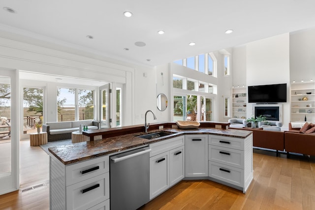 kitchen with a sink, open floor plan, stainless steel dishwasher, light wood finished floors, and dark stone countertops