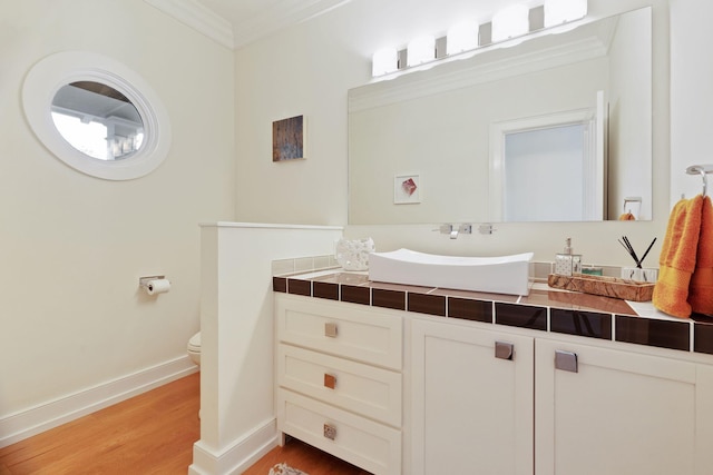 bathroom with baseboards, toilet, wood finished floors, crown molding, and vanity