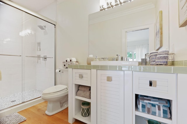 bathroom featuring a stall shower, toilet, ornamental molding, wood finished floors, and vanity