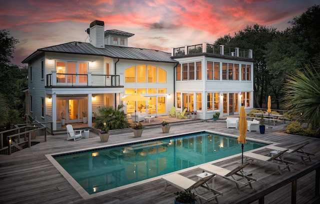 back of property featuring an outdoor pool, a balcony, metal roof, a standing seam roof, and french doors