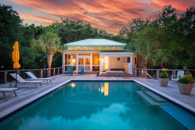 pool at dusk with an outdoor pool, an outdoor structure, a wooden deck, and a storage structure