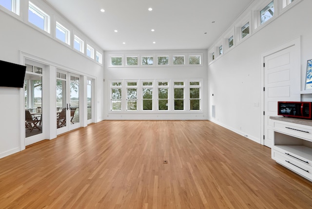 unfurnished living room with baseboards, a high ceiling, french doors, light wood-type flooring, and recessed lighting