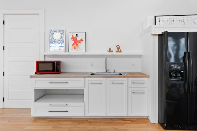 bar with a sink, light wood-style flooring, and black fridge