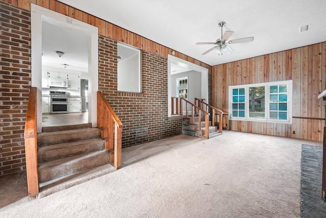 carpeted living room featuring a wealth of natural light, ceiling fan, brick wall, and wood walls