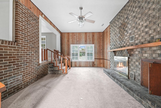 unfurnished living room featuring carpet floors, a brick fireplace, wooden walls, and brick wall