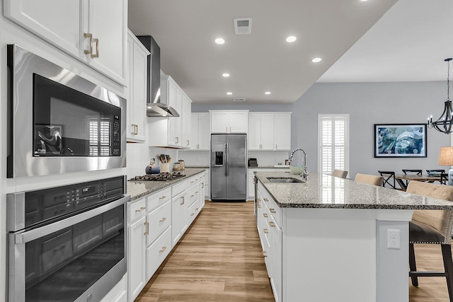 kitchen featuring appliances with stainless steel finishes, white cabinetry, sink, a kitchen breakfast bar, and wall chimney range hood