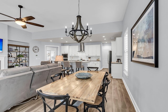 dining room with sink, ceiling fan with notable chandelier, and light hardwood / wood-style flooring