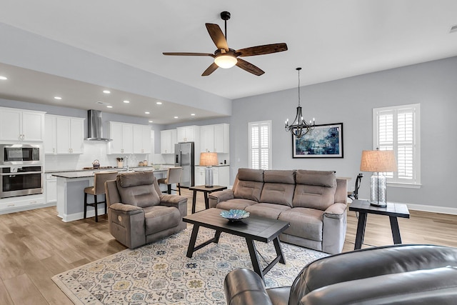 living room featuring ceiling fan with notable chandelier and light hardwood / wood-style floors