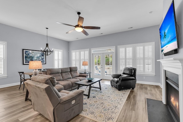 living room with ceiling fan with notable chandelier, light hardwood / wood-style flooring, and french doors