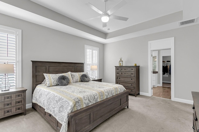 bedroom with light carpet, ceiling fan, and a tray ceiling