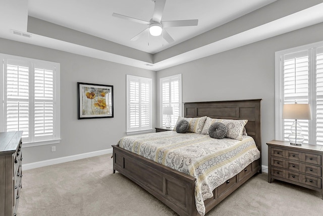 carpeted bedroom with a raised ceiling and ceiling fan