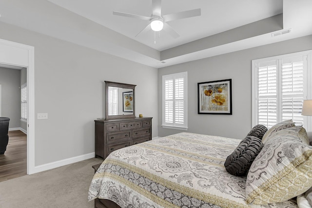 bedroom with ceiling fan, a raised ceiling, and light carpet