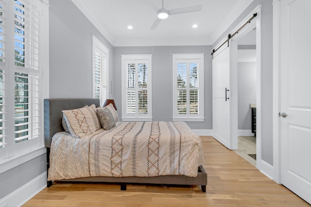 bedroom with hardwood / wood-style flooring, ceiling fan, a barn door, and ornamental molding