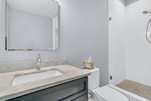 bathroom featuring toilet, a tile shower, and vanity