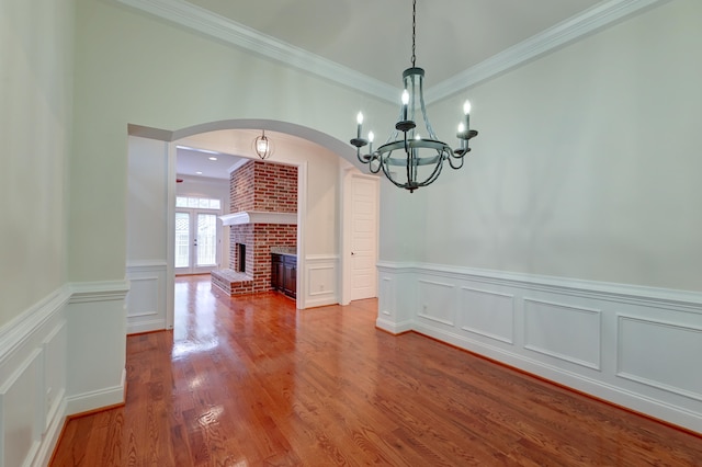 unfurnished dining area with a brick fireplace, hardwood / wood-style flooring, crown molding, and a notable chandelier