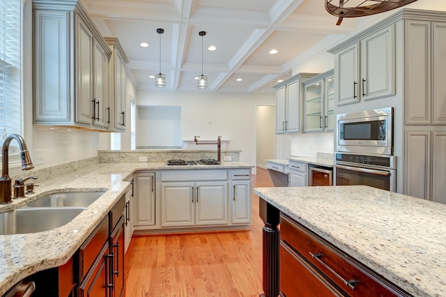 kitchen featuring appliances with stainless steel finishes, beam ceiling, hanging light fixtures, sink, and light hardwood / wood-style floors