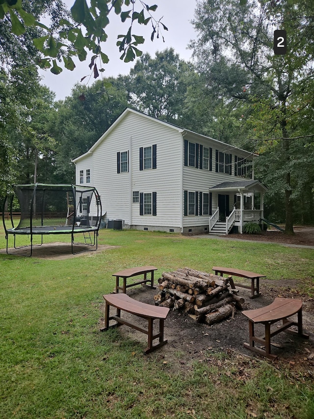 back of house with a trampoline and a lawn