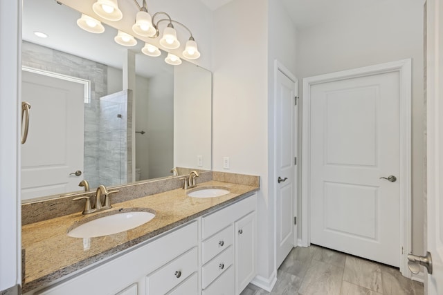 full bathroom featuring double vanity, a tile shower, and a sink