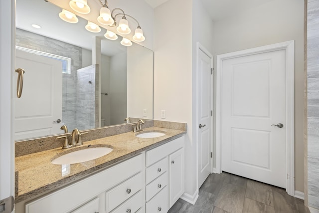 full bathroom featuring baseboards, double vanity, a sink, and a tile shower