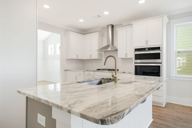 kitchen featuring wall chimney range hood, light hardwood / wood-style flooring, white cabinetry, light stone counters, and tasteful backsplash