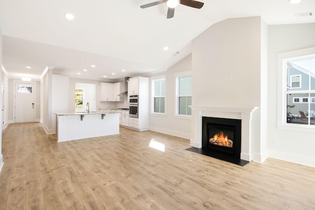 unfurnished living room featuring plenty of natural light, lofted ceiling, light wood-type flooring, and sink