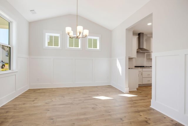 unfurnished dining area with light hardwood / wood-style floors, a notable chandelier, lofted ceiling, and plenty of natural light