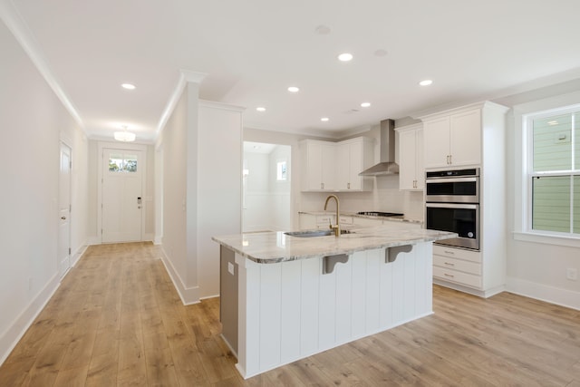 kitchen with light stone counters, white cabinetry, wall chimney exhaust hood, double oven, and sink