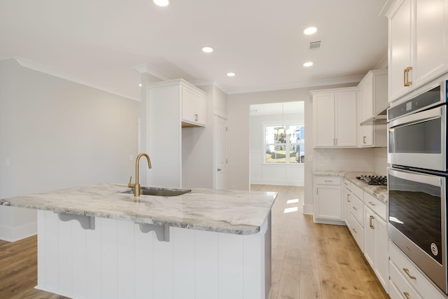 kitchen with a kitchen island with sink, sink, light wood-type flooring, white cabinetry, and light stone counters