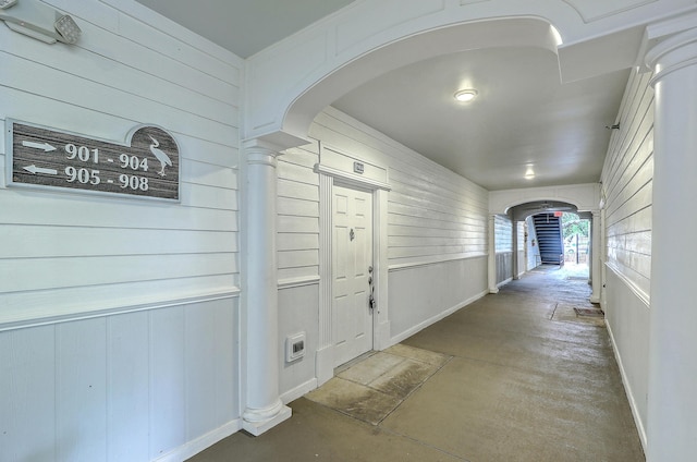 corridor featuring concrete flooring, wooden walls, arched walkways, and baseboards