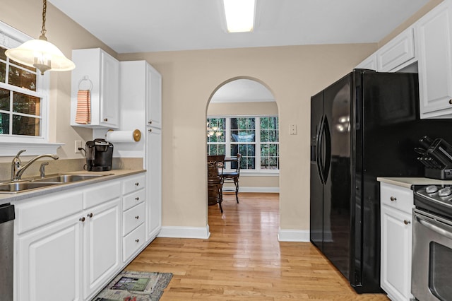 kitchen with sink, hanging light fixtures, light wood-type flooring, appliances with stainless steel finishes, and white cabinetry