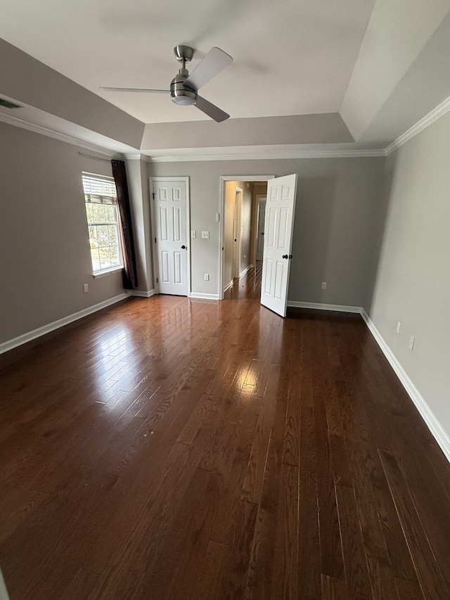 unfurnished bedroom with ceiling fan, ornamental molding, a tray ceiling, and dark hardwood / wood-style flooring