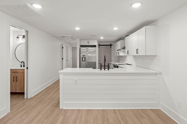 kitchen featuring white cabinetry, sink, stainless steel fridge with ice dispenser, kitchen peninsula, and light hardwood / wood-style floors