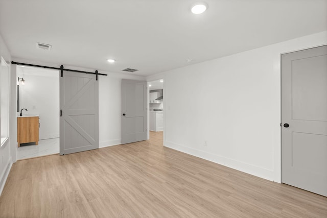 unfurnished bedroom with a barn door and light wood-type flooring