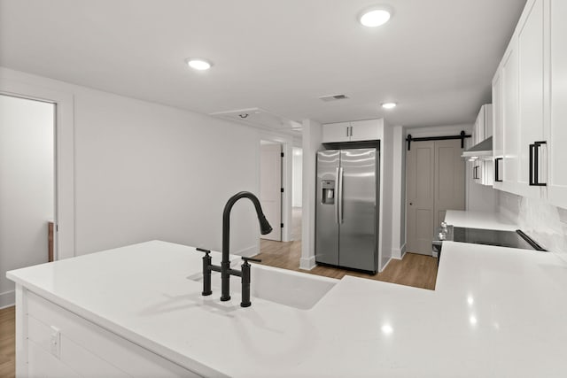 kitchen featuring white cabinets, sink, decorative backsplash, stainless steel fridge, and a barn door