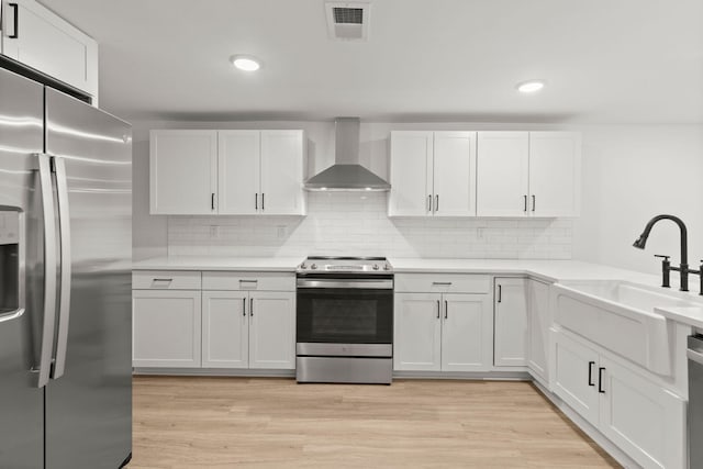 kitchen featuring white cabinets, light wood-type flooring, wall chimney range hood, and appliances with stainless steel finishes