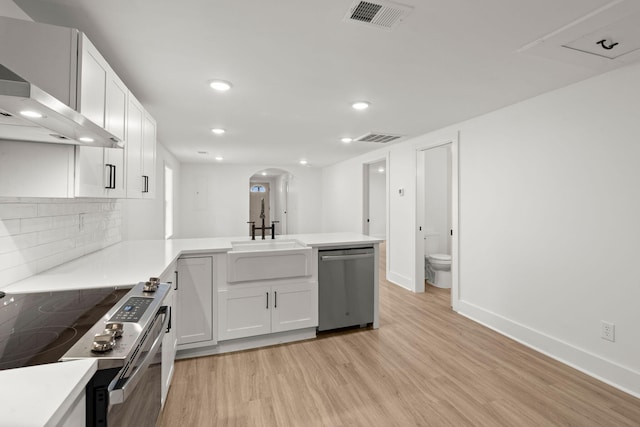 kitchen with white cabinetry, sink, stainless steel appliances, wall chimney range hood, and kitchen peninsula