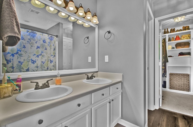 bathroom featuring wood finished floors, visible vents, a sink, and double vanity