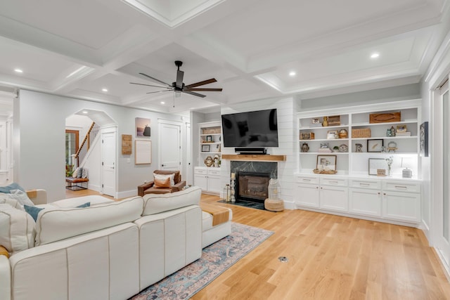 living room with coffered ceiling, light wood-type flooring, a high end fireplace, and ceiling fan