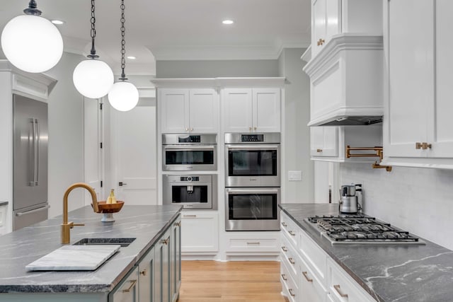 kitchen featuring light hardwood / wood-style floors, stainless steel appliances, a center island with sink, tasteful backsplash, and ornamental molding