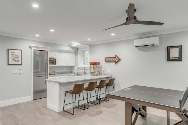 kitchen with white cabinetry, a wall unit AC, kitchen peninsula, built in appliances, and a kitchen bar