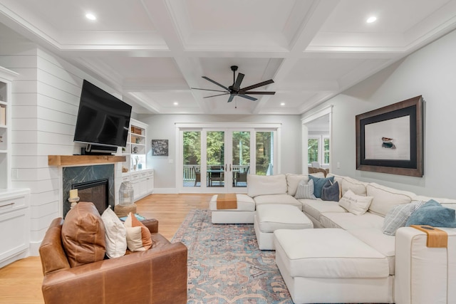 living room featuring coffered ceiling, ceiling fan, a fireplace, and light wood-type flooring