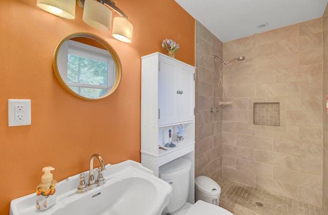 bathroom featuring a tile shower, sink, and toilet