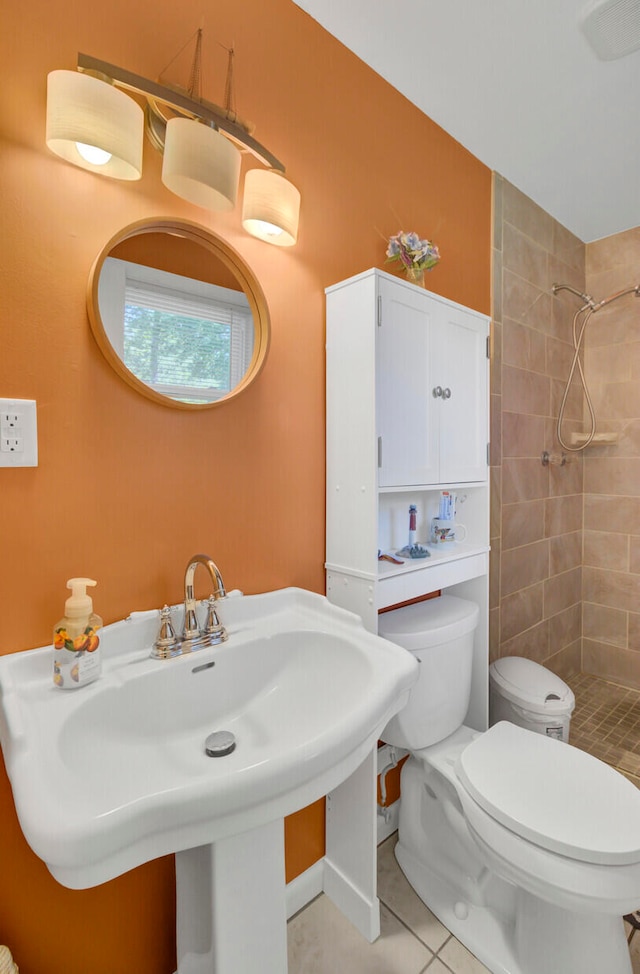 bathroom with a tile shower, toilet, sink, and tile patterned floors