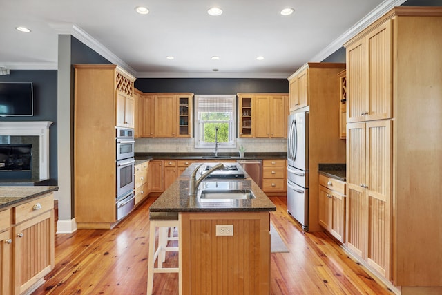 kitchen featuring light hardwood / wood-style floors, crown molding, an island with sink, and stainless steel appliances