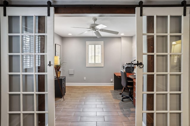 home office featuring ceiling fan, light hardwood / wood-style floors, and a barn door