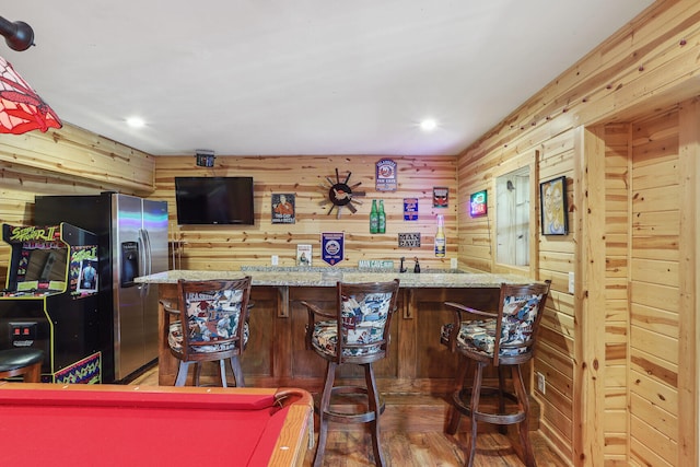 bar featuring stainless steel fridge, light stone counters, wood walls, hardwood / wood-style floors, and pool table