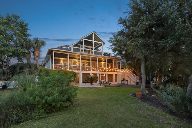 back house at dusk with a yard, a patio, a balcony, and ceiling fan